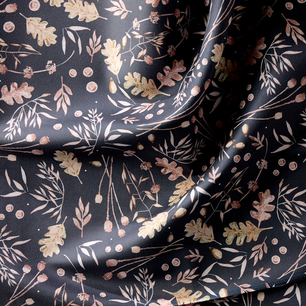 A close-up of dark fabric with a pattern of muted autumn leaves, acorns, and botanical sprigs.