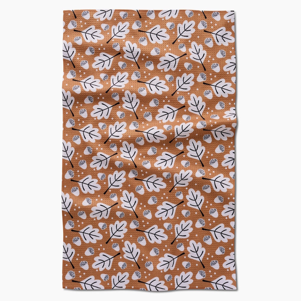 A flat-lay view of an orange tea towel with a repeating pattern of white oak leaves and small acorns.