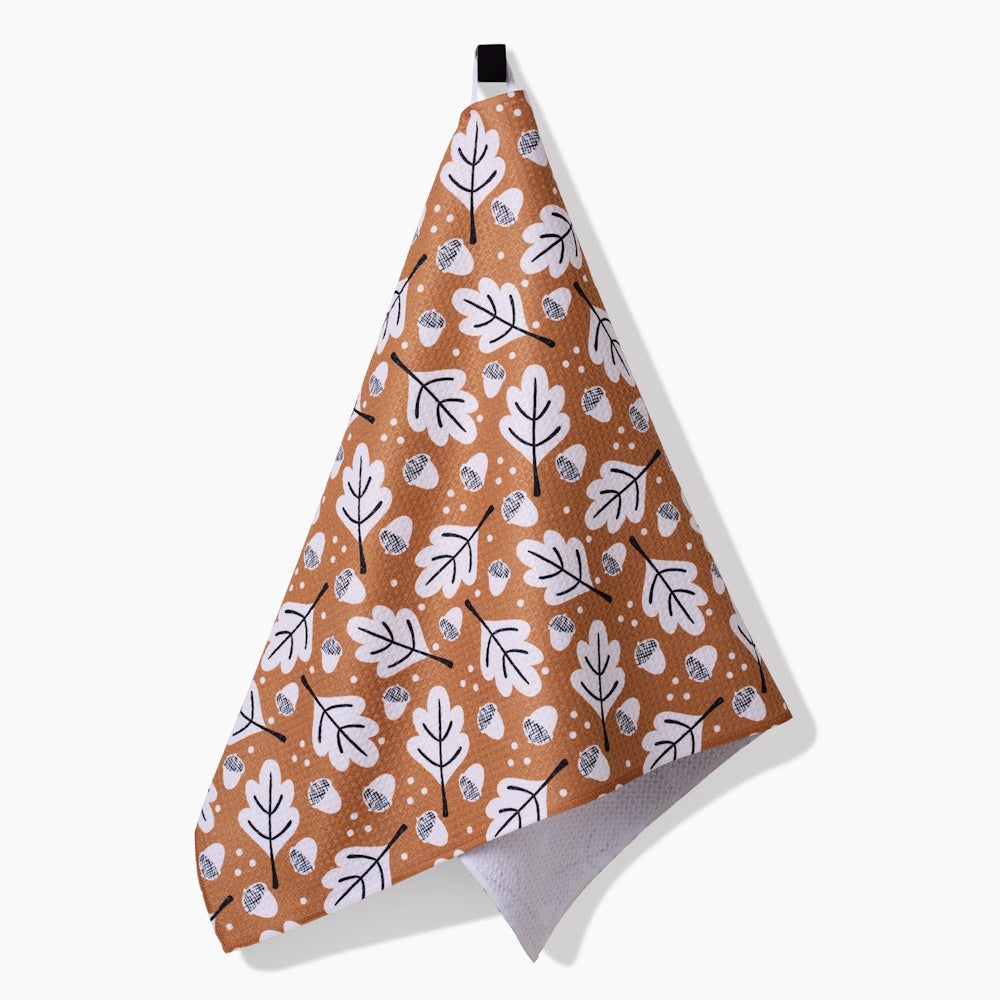 A hanging brown tea towel patterned with white leaves, small acorns, and dots, showing a white underside.