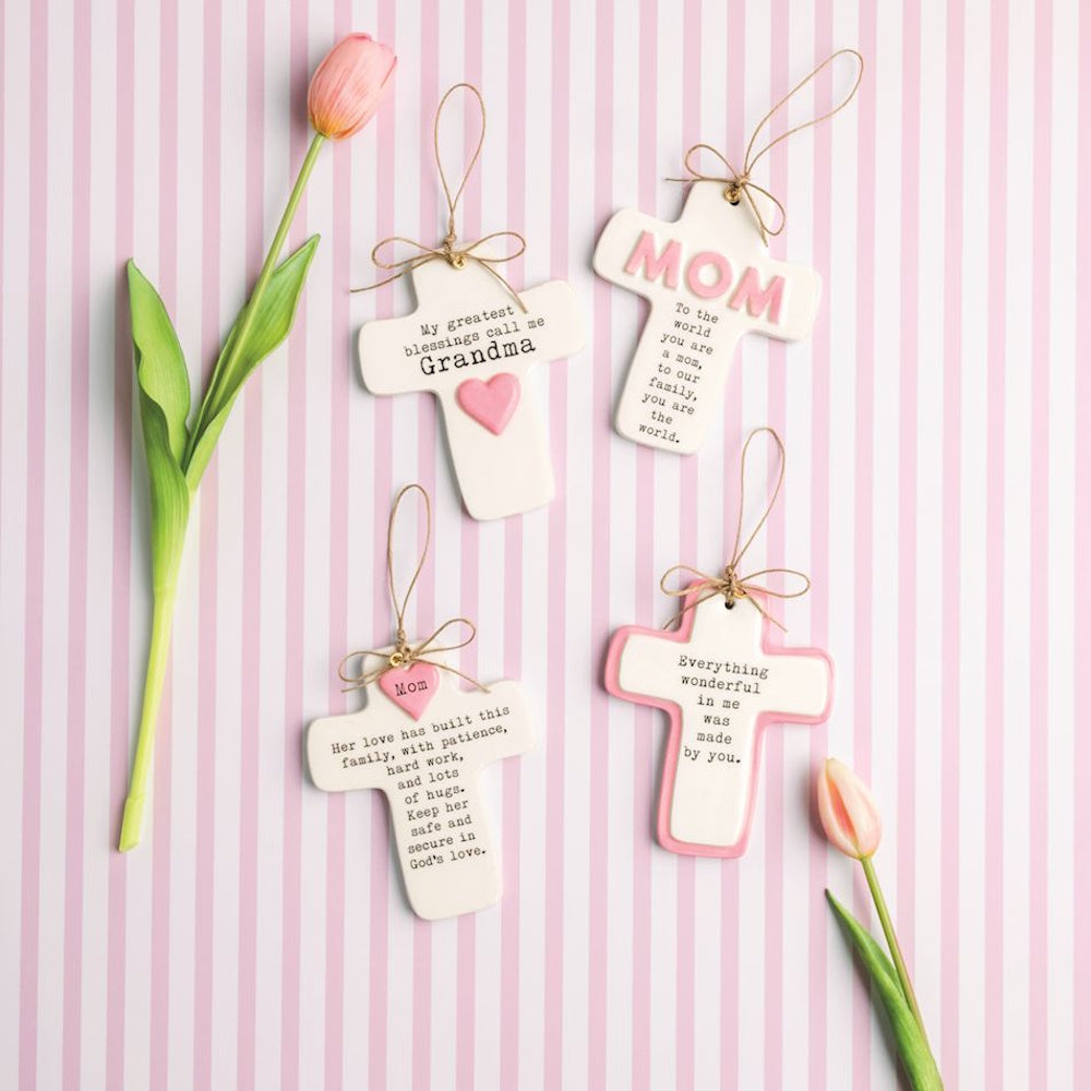 Four decorative ceramic crosses with sentimental messages for Mom and Grandma on a pink striped background.