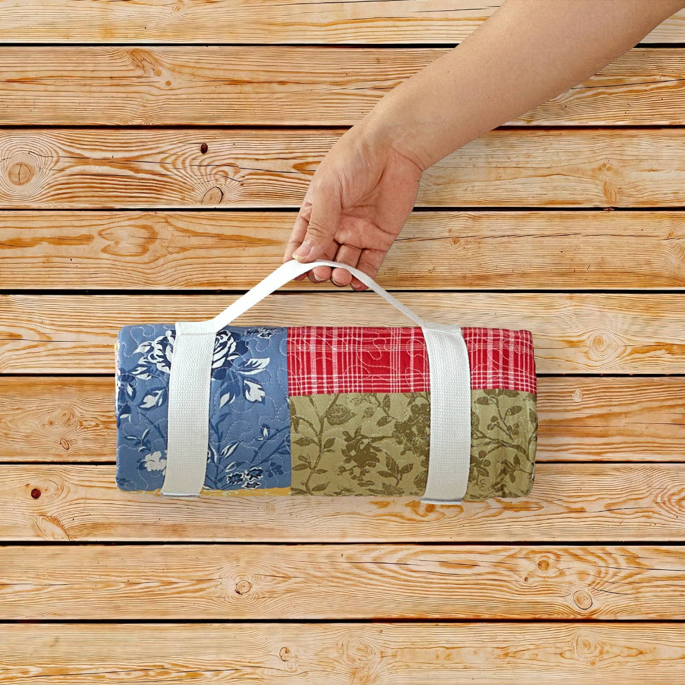 Hand holding a rolled floral patchwork quilt with a white carry strap on a rustic light wood plank background.