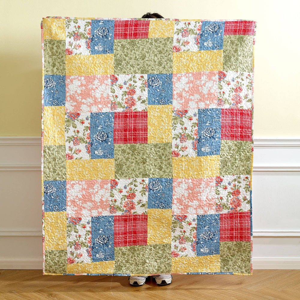 Colorful farmhouse floral patchwork quilt with rose patterns and plaid squares in yellow, blue, red, and green.
