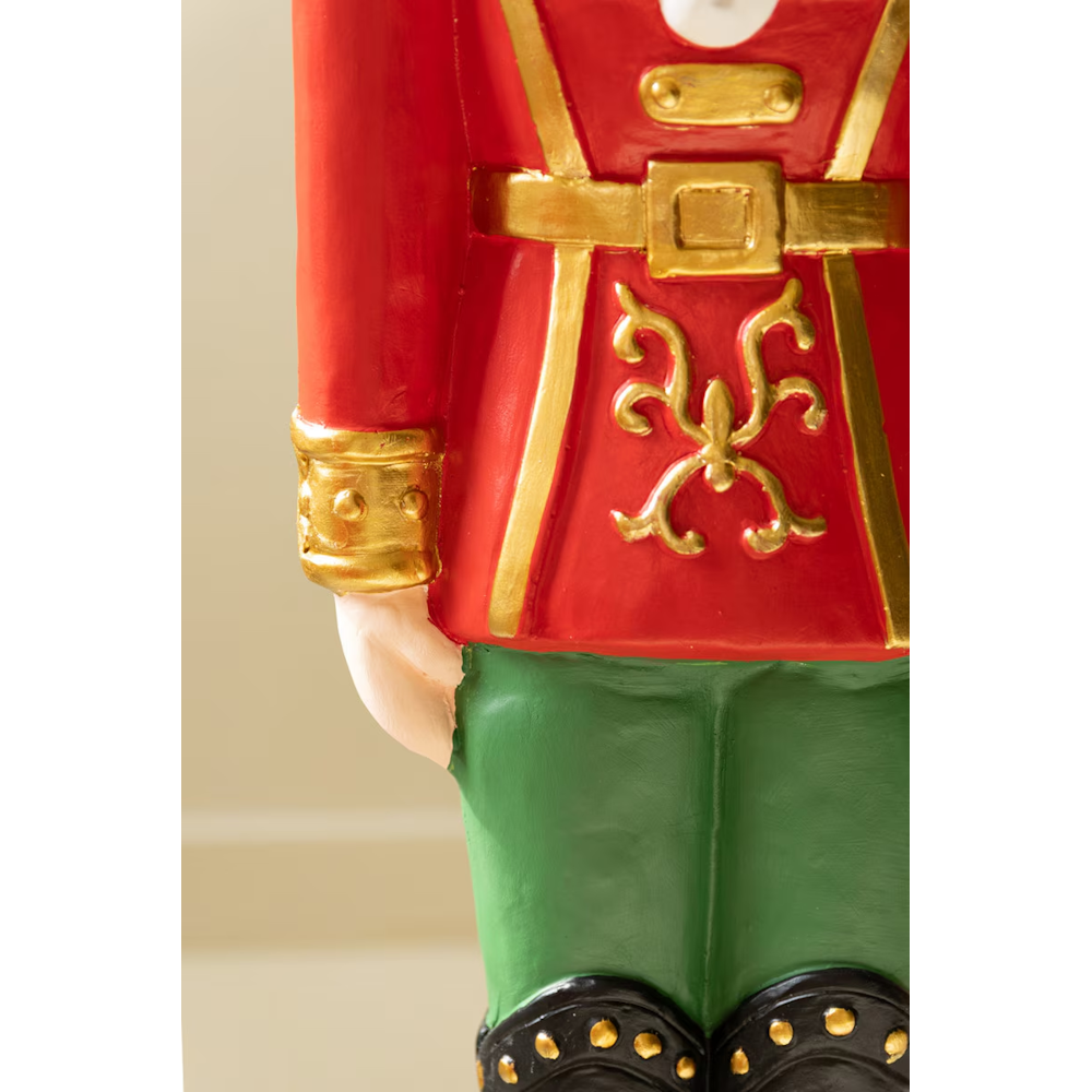 Close-up of the red coat, gold trim belt, and green pants of a faux concrete nutcracker statue.