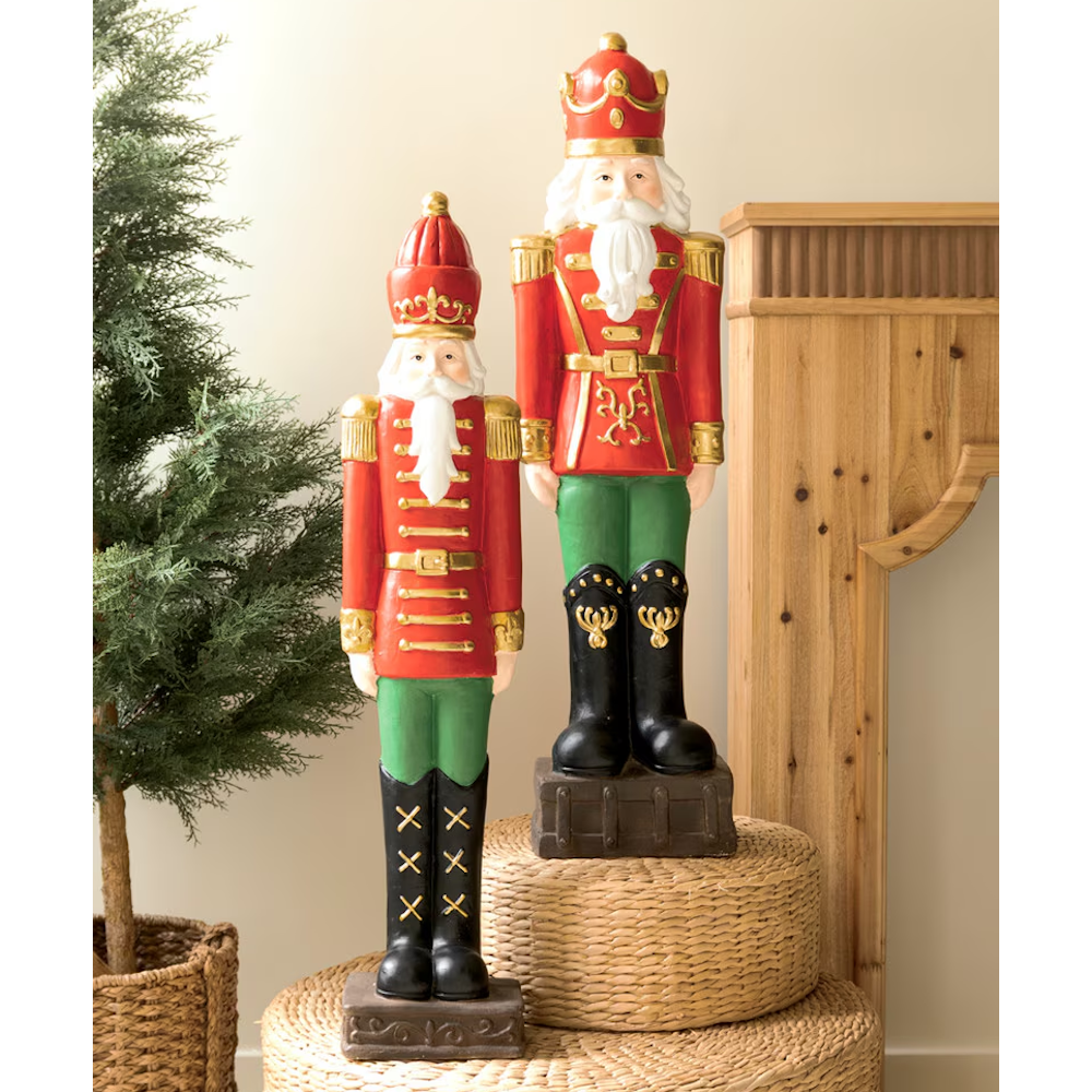 Two faux concrete Christmas nutcracker soldier statues dressed in red, green, and gold uniforms.