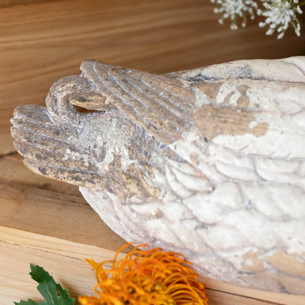 Close-up of the textured tail feathers of a weathered pintail duck statue resting on wood.