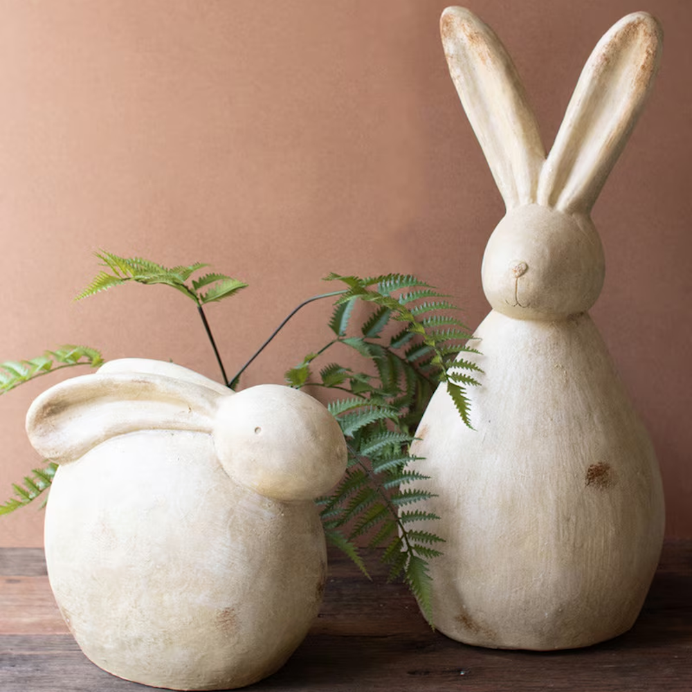 Pair of minimalist faux stone rabbit sculptures in sitting and standing poses with rustic weathered finish and fern accents.
