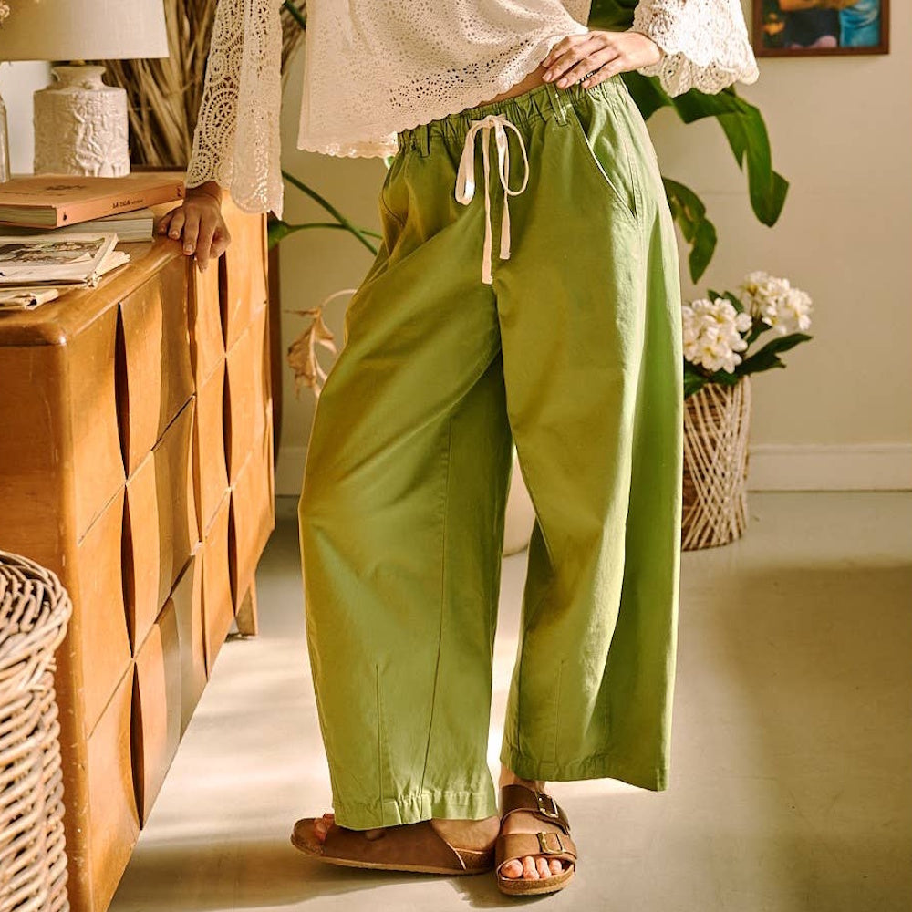 Woman wearing fern green wide barrel leg pants with a drawstring elastic waist and brown slide sandals.