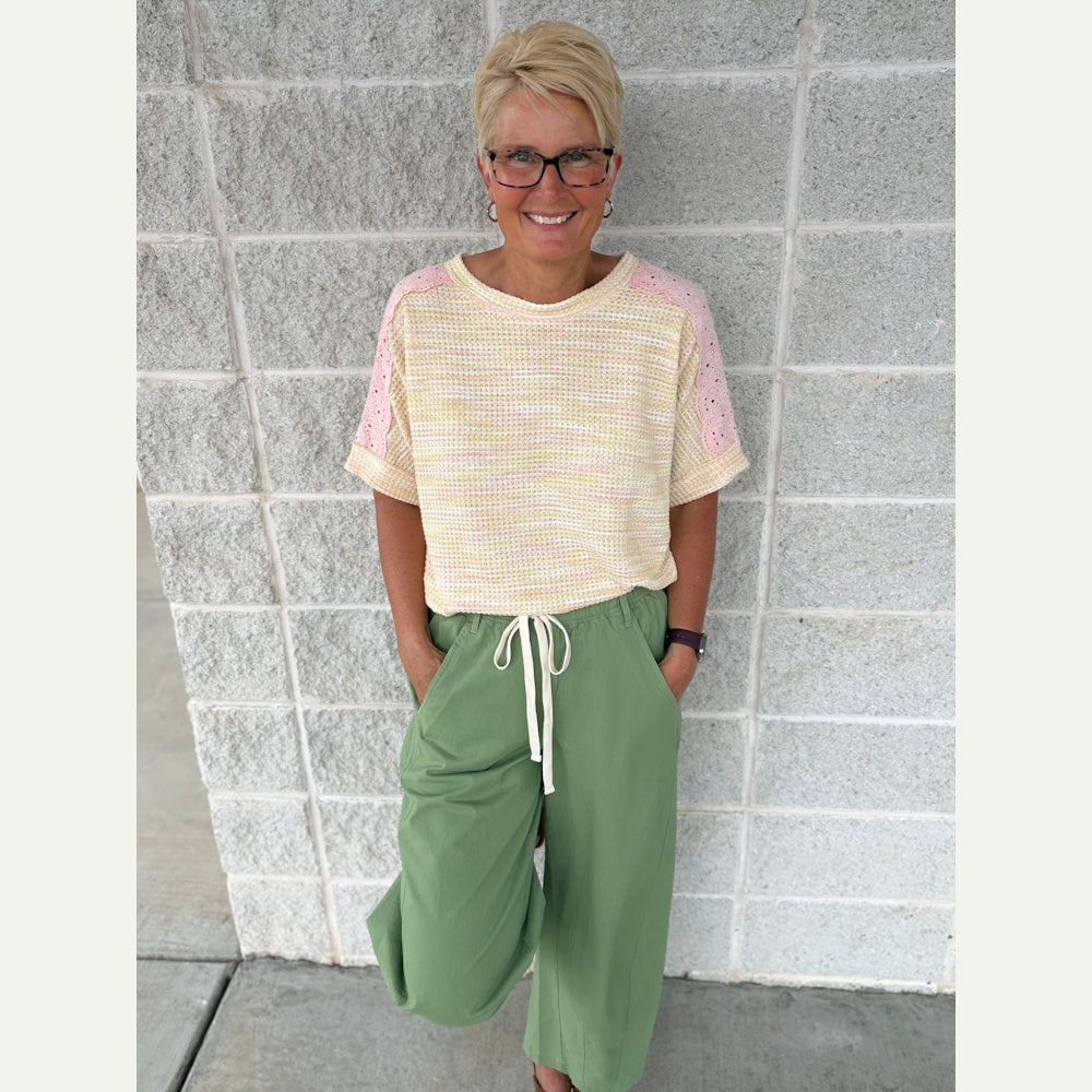 Woman wearing fern green wide barrel leg pants with a drawstring waist and a yellow textured short-sleeve top.