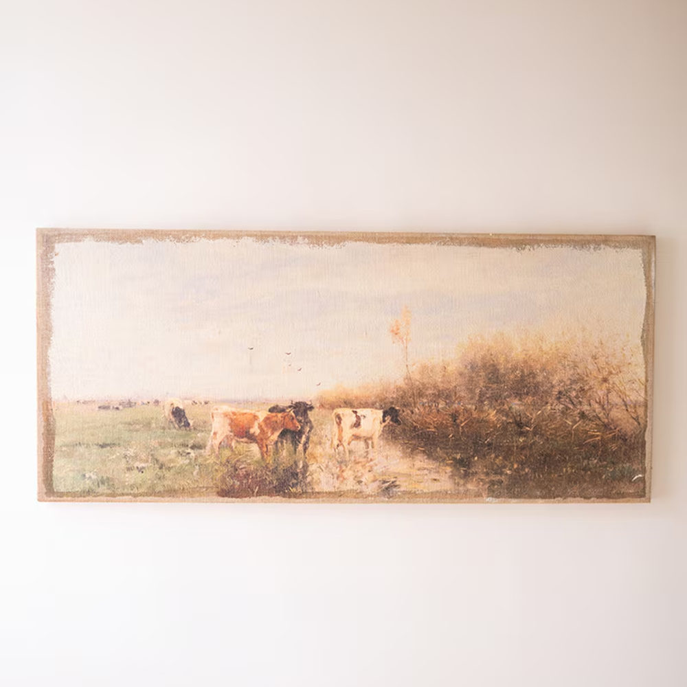 Panoramic pastoral canvas print on burlap depicting cows grazing in a meadow, hung on a light beige wall.