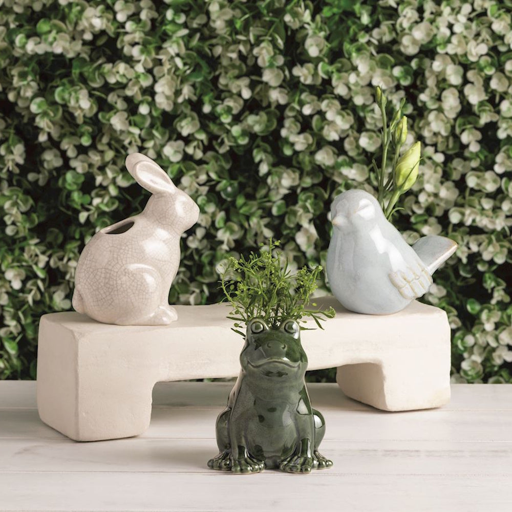 Small ceramic animal bud vases featuring a rabbit, frog, and bird holding greenery against a leafy background.