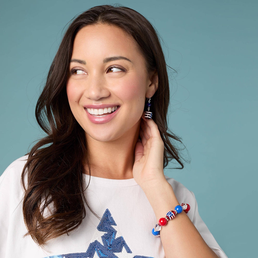 Smiling woman wearing a patriotic red, white, and blue beaded American flag bracelet and matching earrings.