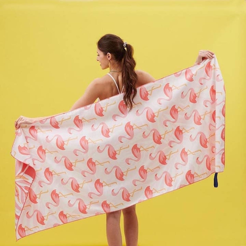 Woman from behind holding up a large white towel with a pink flamingo pattern against a yellow background.