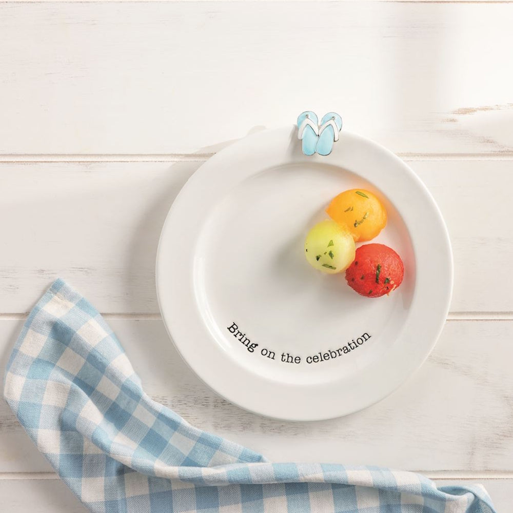 White Mud Pie serving plate with "Bring on the celebration" text, melon balls, and a blue flip flop decorative charm.