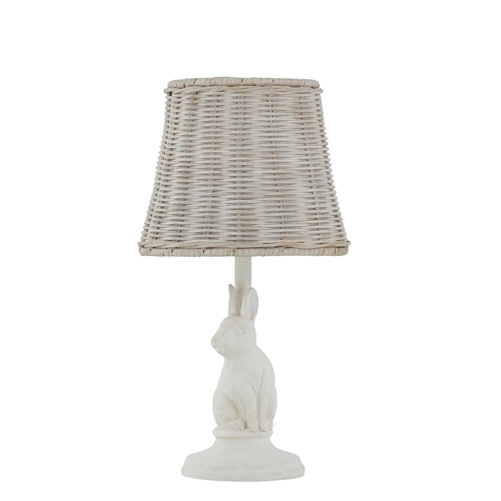 White bunny rabbit table lamp with a woven wicker shade on a neutral stone-like base for nursery or cottage decor.
