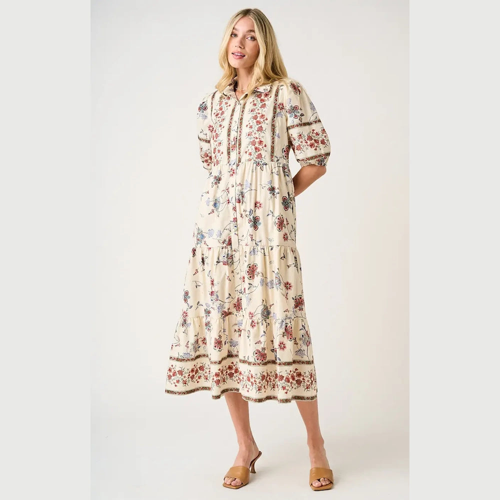 Woman wearing a floral print tiered maxi shirt dress with puff sleeves and tan mule sandals against a white background.