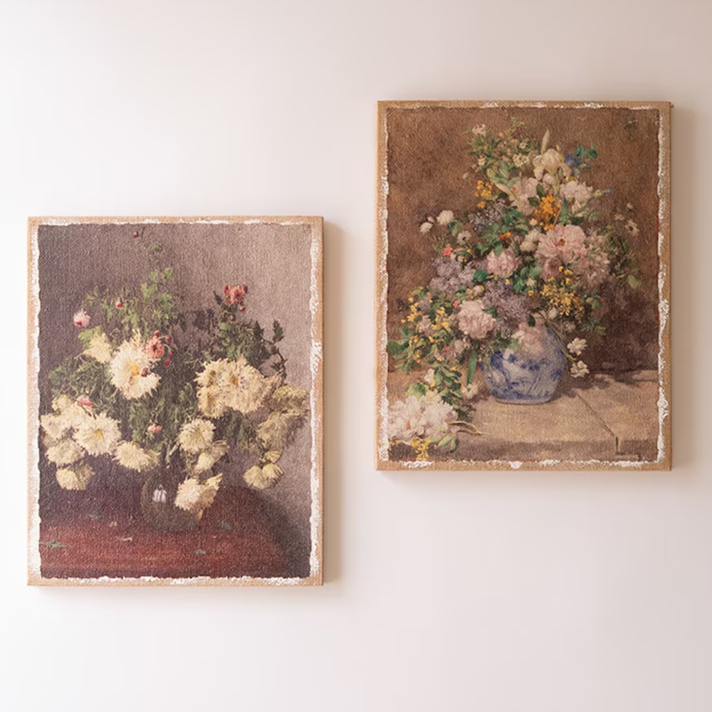 Two vintage floral canvas prints on burlap with distressed white borders hanging on a off-white wall.