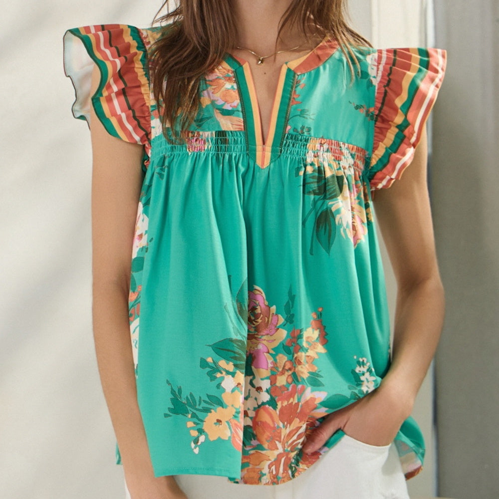 A person wearing a green floral blouse with multi-colored striped ruffle sleeves and white pants.