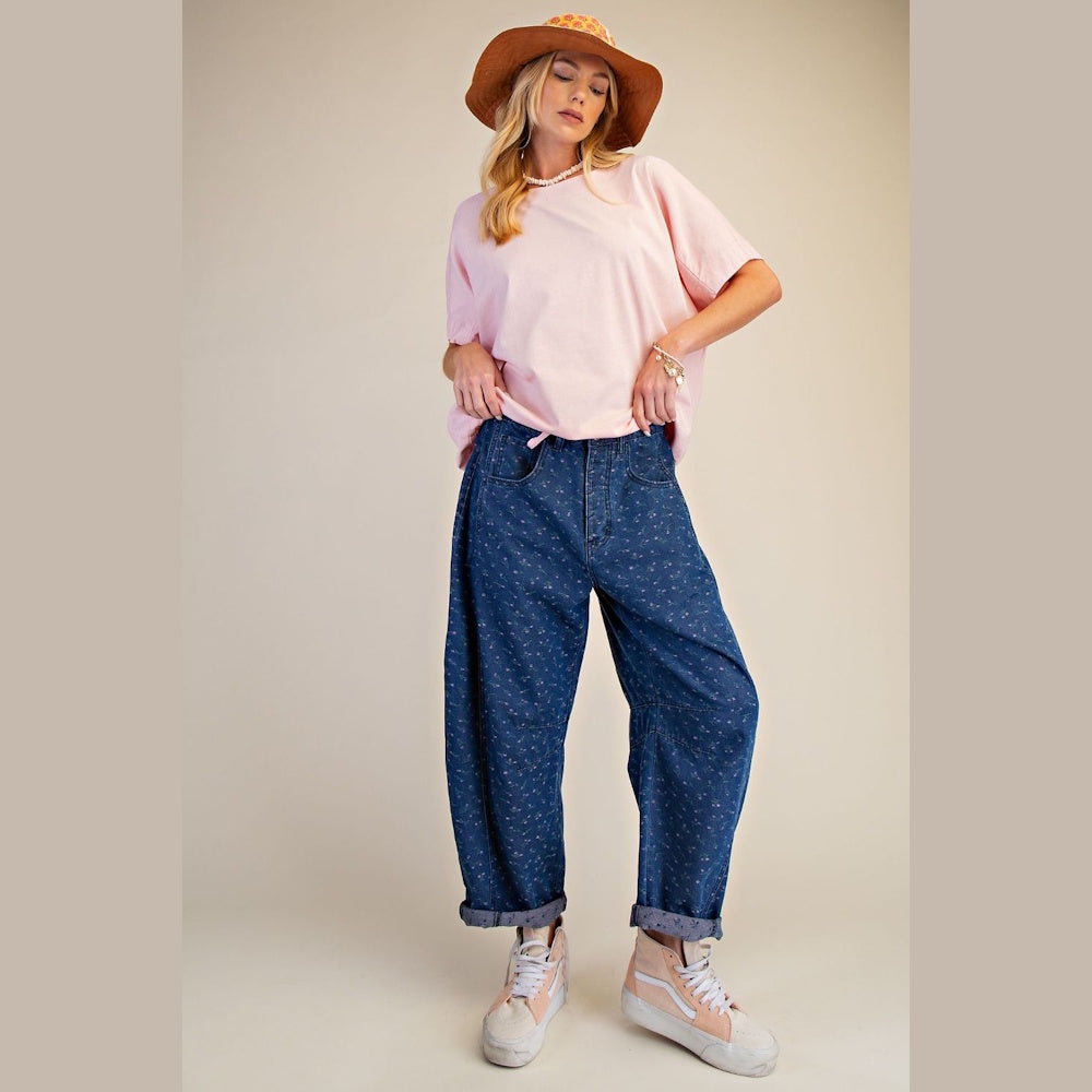 Model in pink t-shirt and blue floral print barrel denim pants with a brown hat and high-top sneakers.