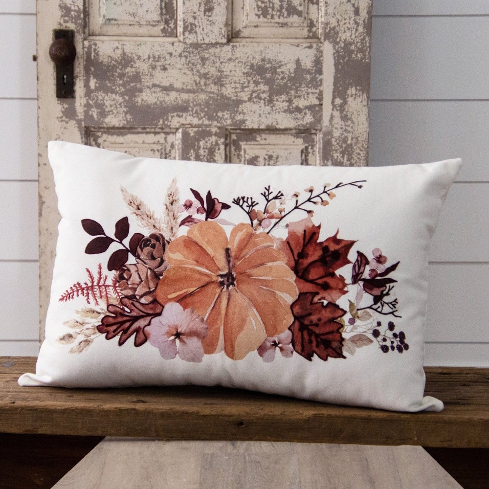 White pillow printed with an autumn arrangement of an orange pumpkin, flowers, and leaves.