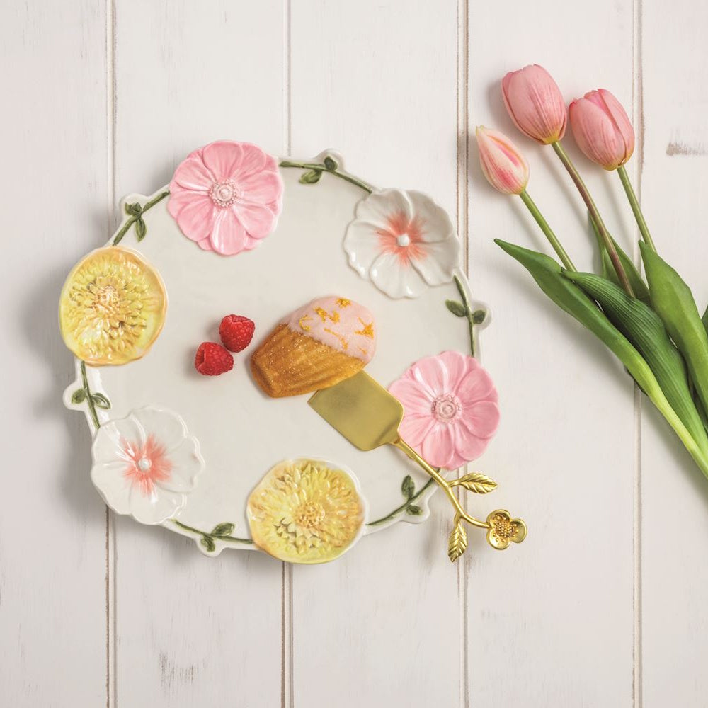 Floral ceramic serving platter with 3D pink and yellow flowers, a gold server, a madeleine, and pink tulips.