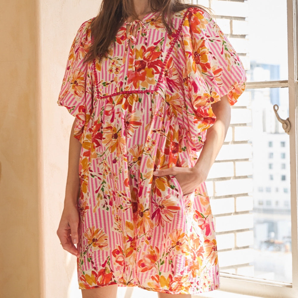 Woman wearing a pink-and-white striped babydoll dress with vibrant floral print and pockets.