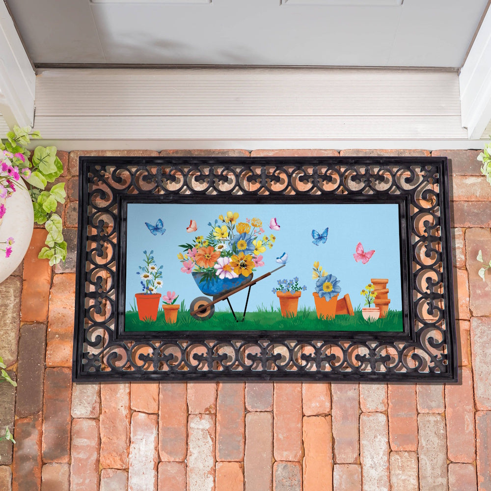 Floral wheelbarrow doormat with colorful potted flowers and butterflies on a brick porch. 116 characters.