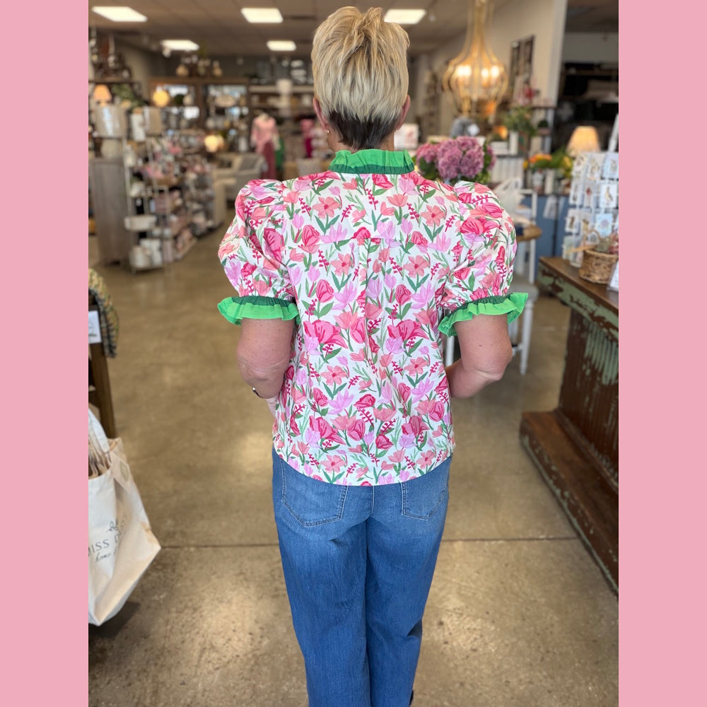 Pink floral puff sleeve blouse with green ruffle trim, worn with blue jeans in a store setting.