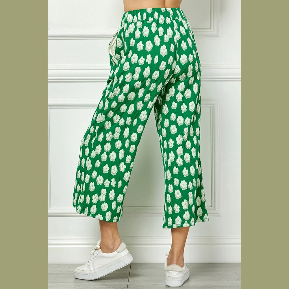 Back view of cropped, wide-leg green pants with a white floral pattern, paired with white sneakers.
