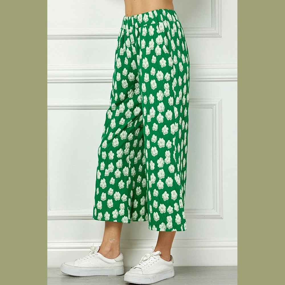 Side view of a person wearing green cropped wide-leg pants with a white floral pattern and white sneakers.