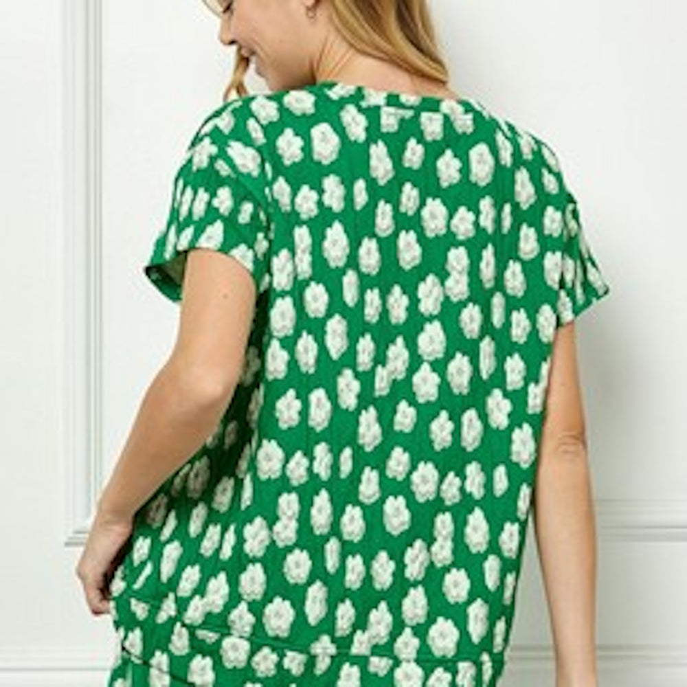Back view of a person wearing a green short-sleeve top with an allover white floral pattern.