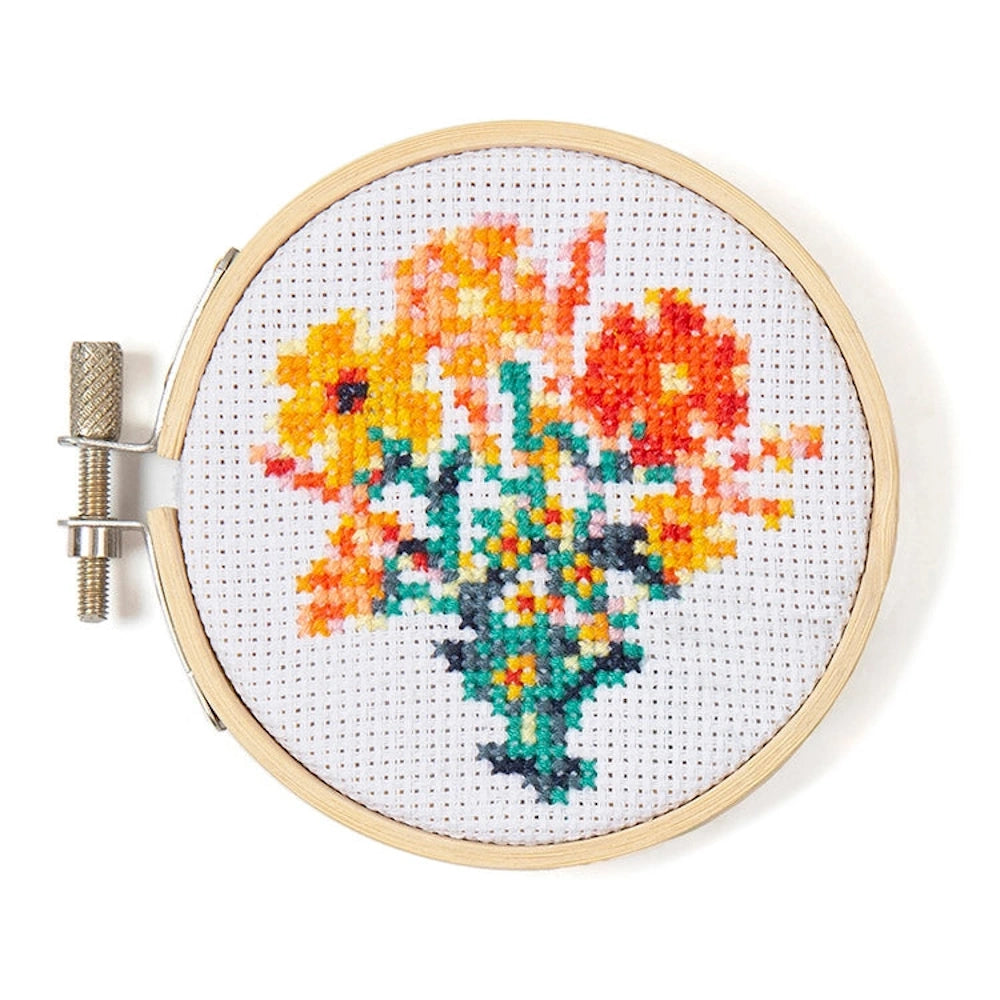 Mini cross-stitch embroidery in a wooden hoop featuring a vibrant bouquet of yellow and orange flowers in a green vase.