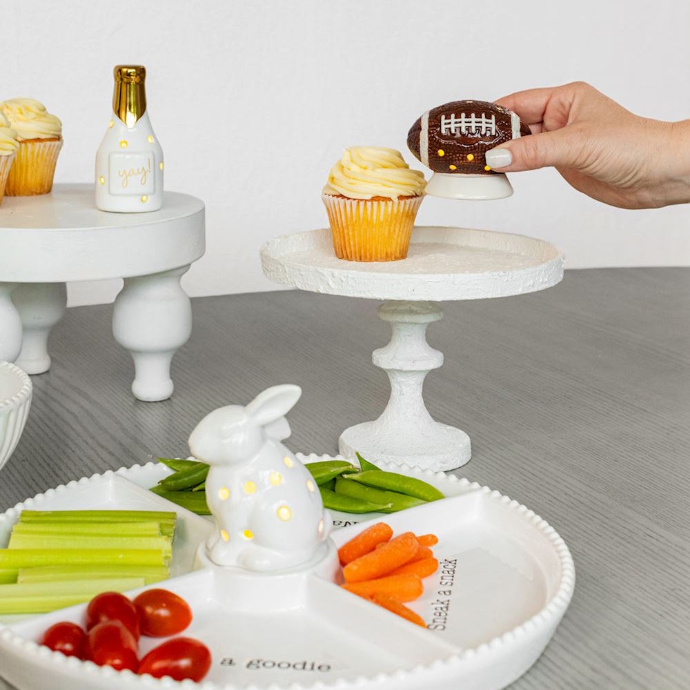 Hand placing a ceramic light-up football figure on a pedestal next to party snacks.