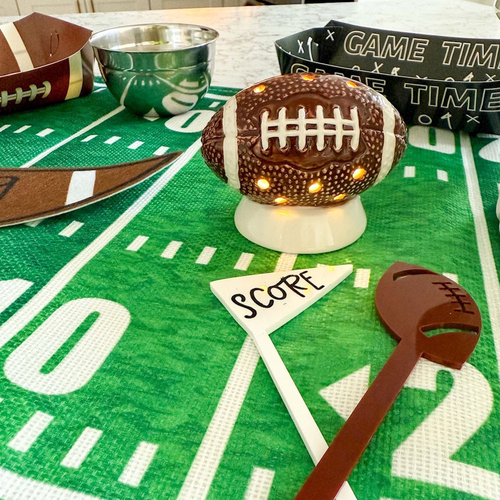 Light-up football ceramic table decor surrounded by game day party decorations on a field runner.