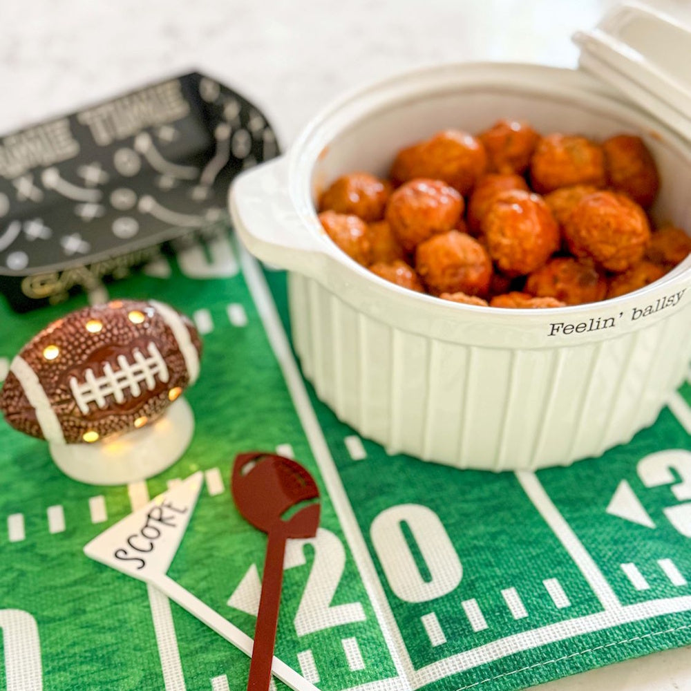 Light-up ceramic football decor on a field mat next to a dish of meatballs for game day.