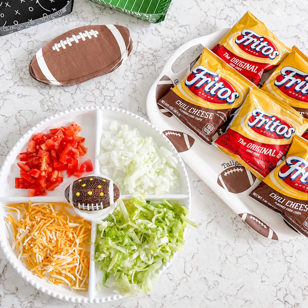 Game day snack setup with divided tray of toppings, small football figurine, and bags of Fritos chips.