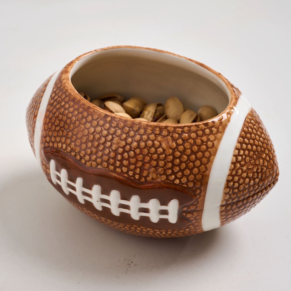A football-shaped ceramic snack bowl filled with pistachios on a white background.