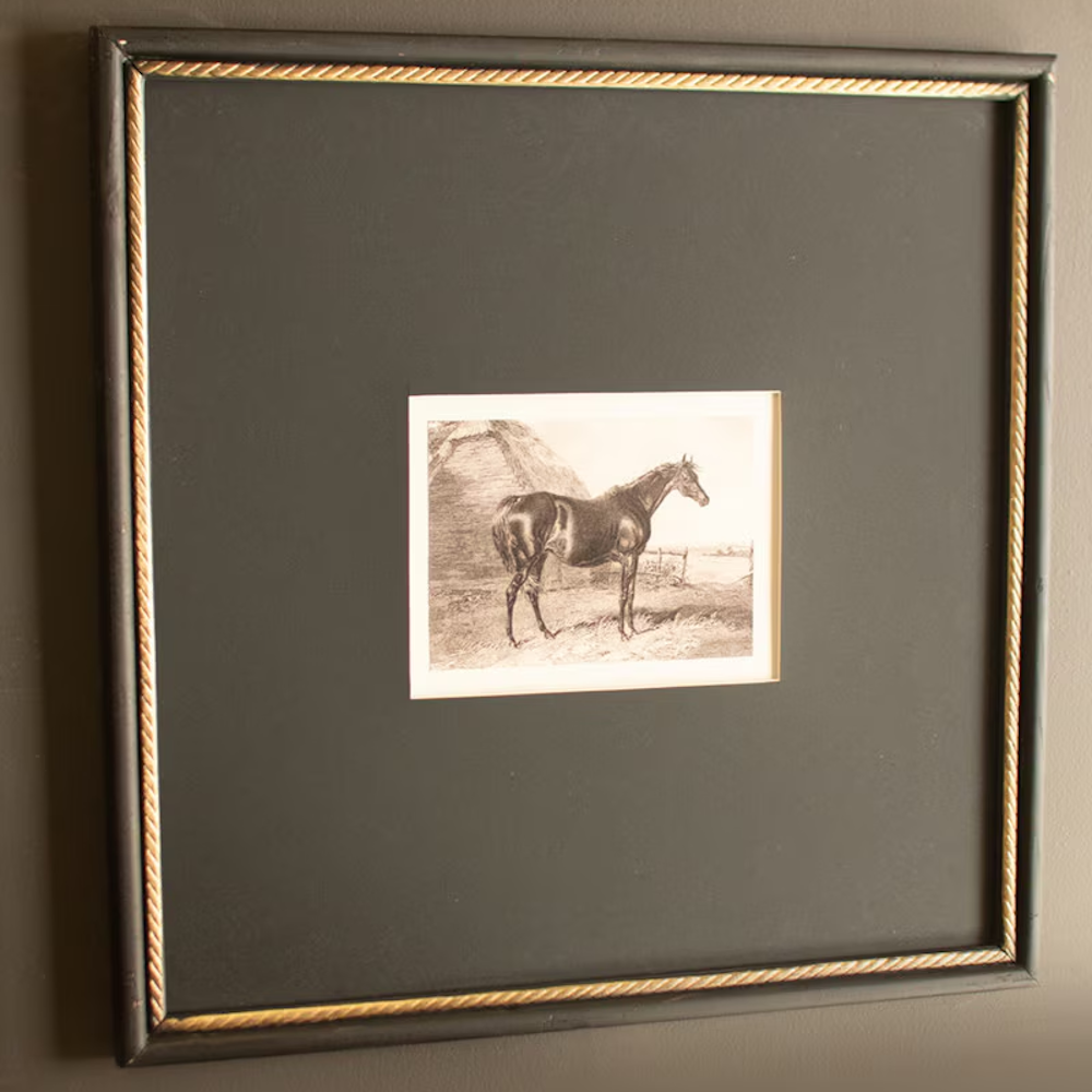 Angled view of a framed vintage horse print featuring a dark mat and gold beaded inner border.