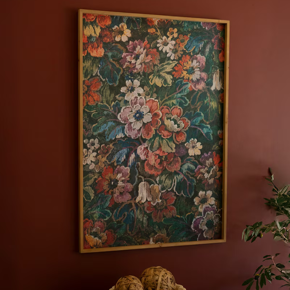 Framed vintage-style floral wall art with muted pink and red flowers on a dark green background, hanging on a burgundy wall.