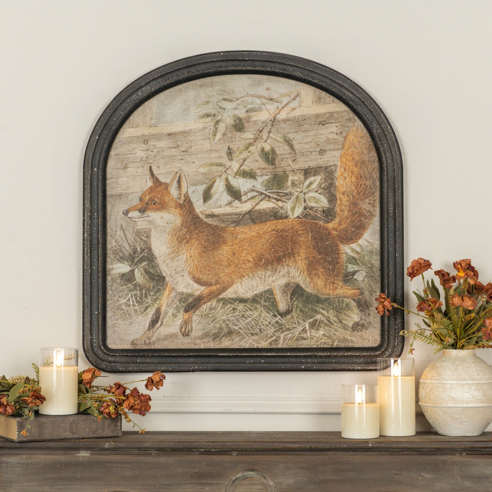 Framed vintage fox art displayed on a mantel with glowing candles and floral accents.