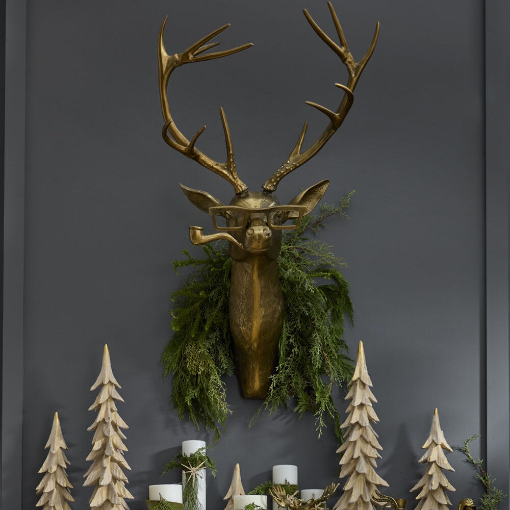 Gold stag head wall mount wearing glasses and a pipe, decorated with a wreath on a dark gray wall.