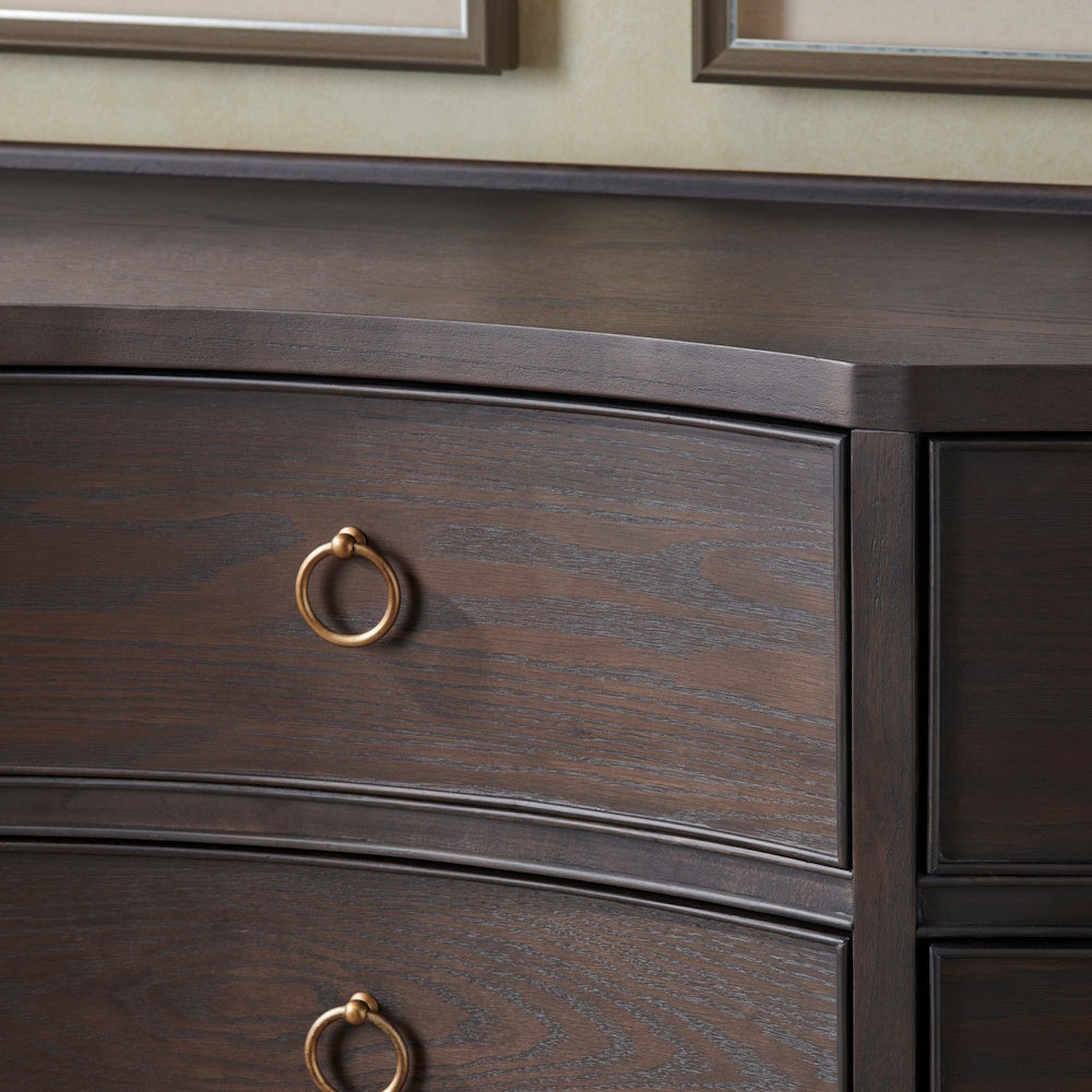 Close-up of a dark wood bow-front dresser featuring textured grain and elegant gold ring pull hardware.