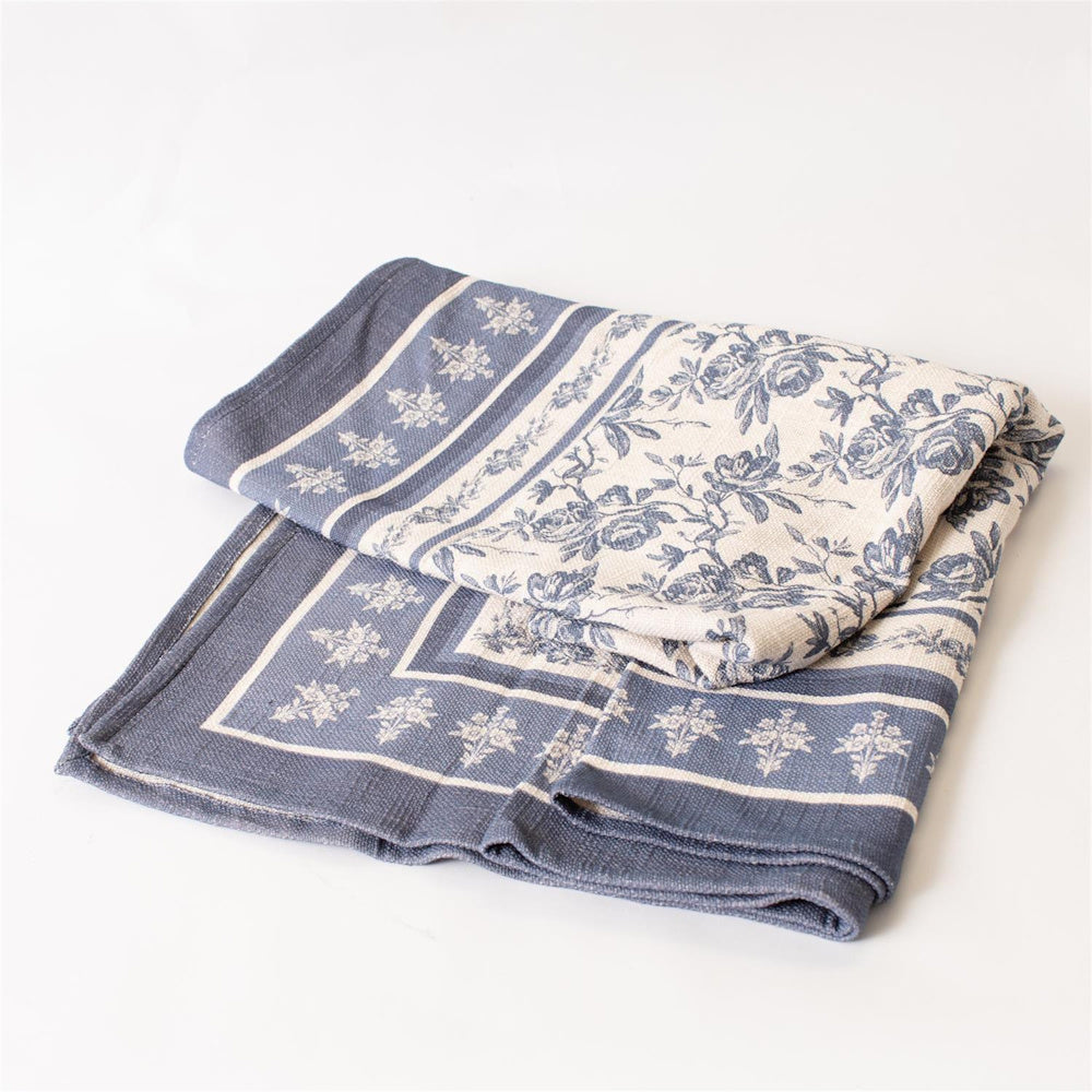Folded French blue and white floral linen tablecloth with a vintage toile pattern and decorative border on a white background.