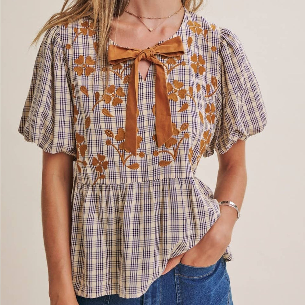 Plaid babydoll blouse with floral embroidery, puff short sleeves, and a bow tie accent at the neckline.
