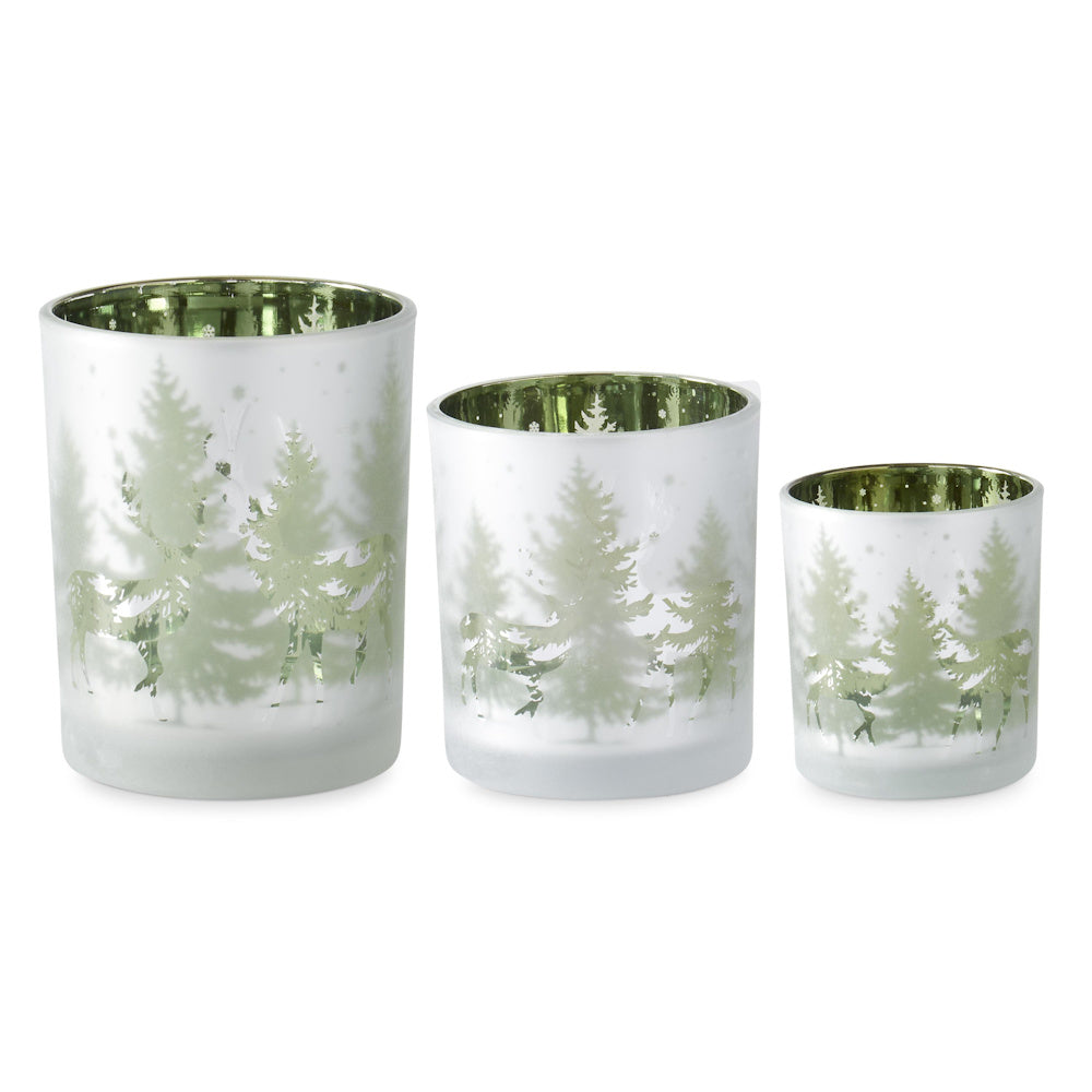 Three frosted glass candle holders with green metallic interiors, featuring pine trees and deer.