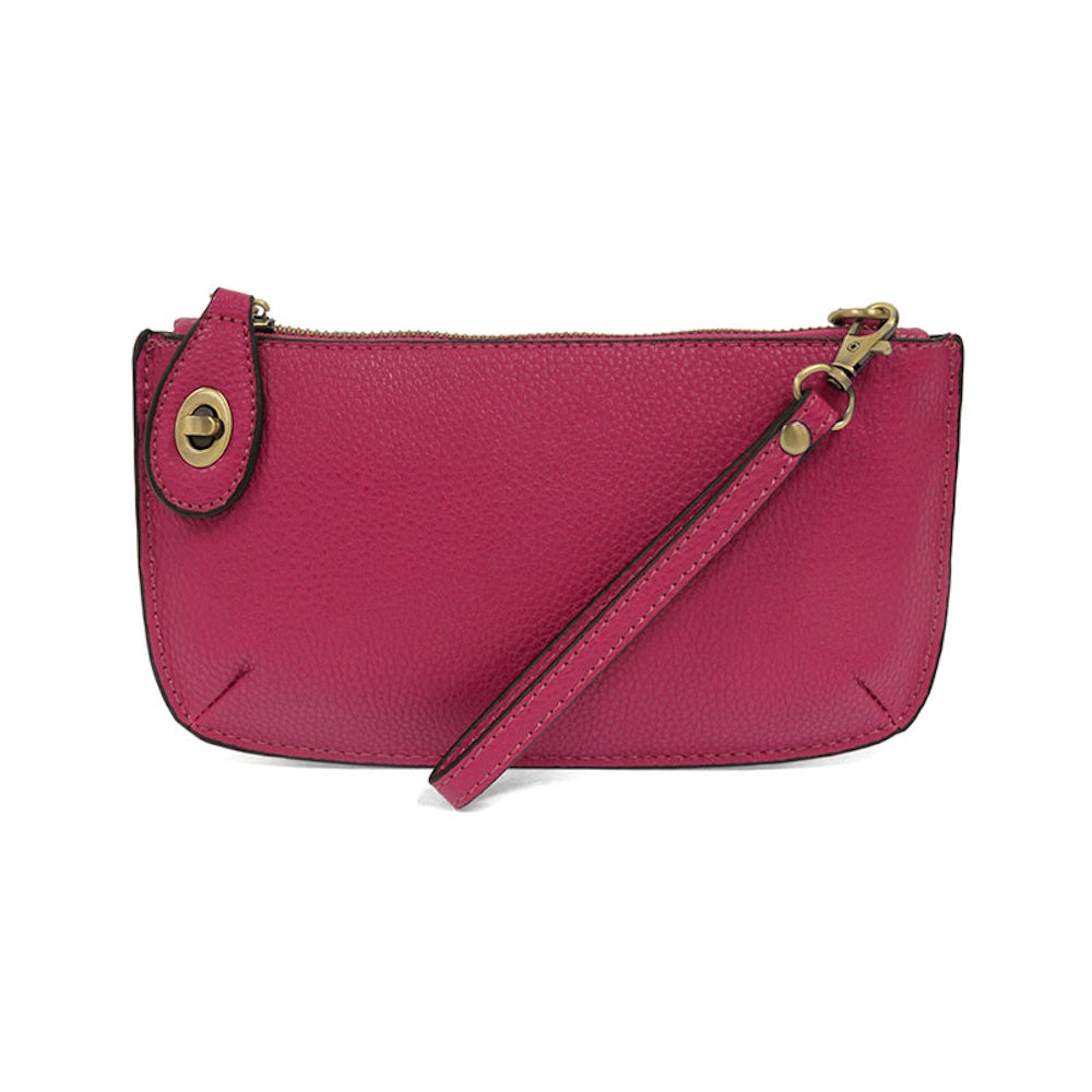 Magenta pink leather wristlet with an antique brass latch clasp and a removable strap on a plain white background.