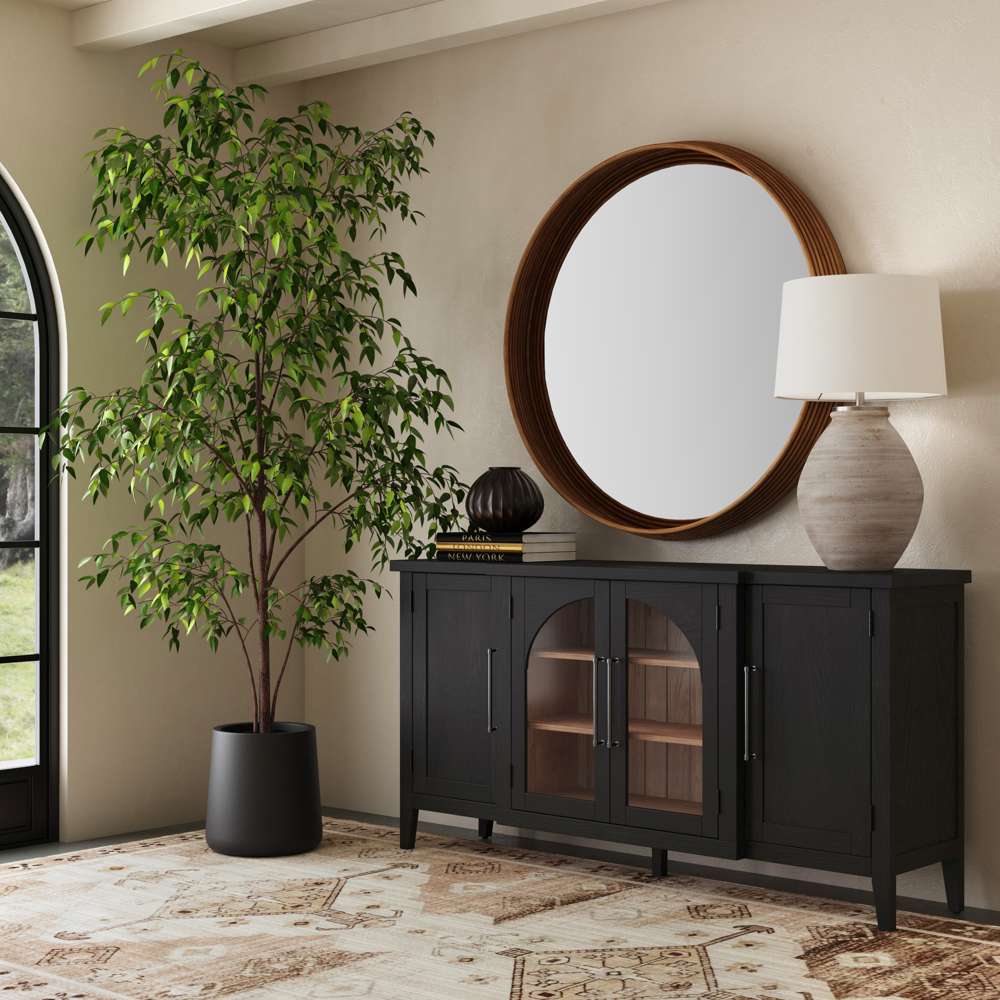 Black sideboard with arched glass doors, a round wood mirror, and a large indoor tree in a modern room.