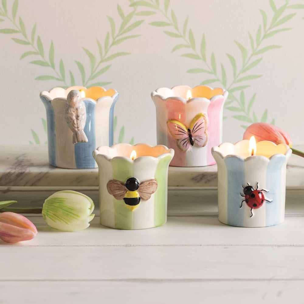 Striped ceramic garden icon candles featuring a bird, butterfly, bee, and ladybug on a white wood surface.