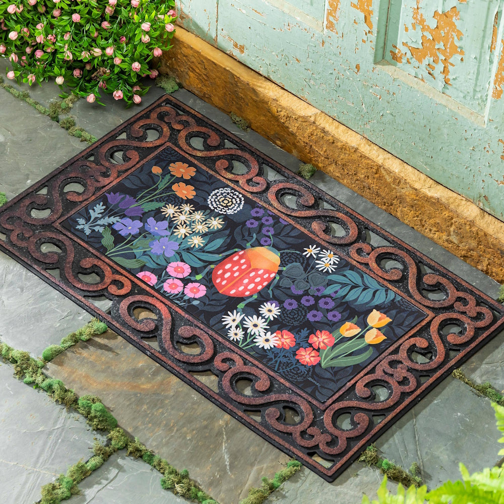 Decorative rubber doormat with a colorful floral and ladybug design on a stone entryway.