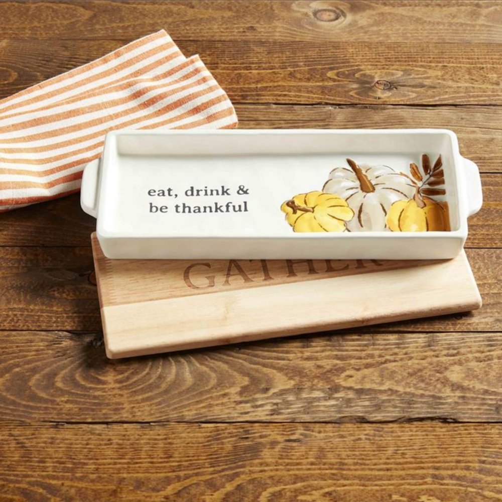 White ceramic tray with pumpkin illustrations and text resting on a wooden board labeled "GATHER".