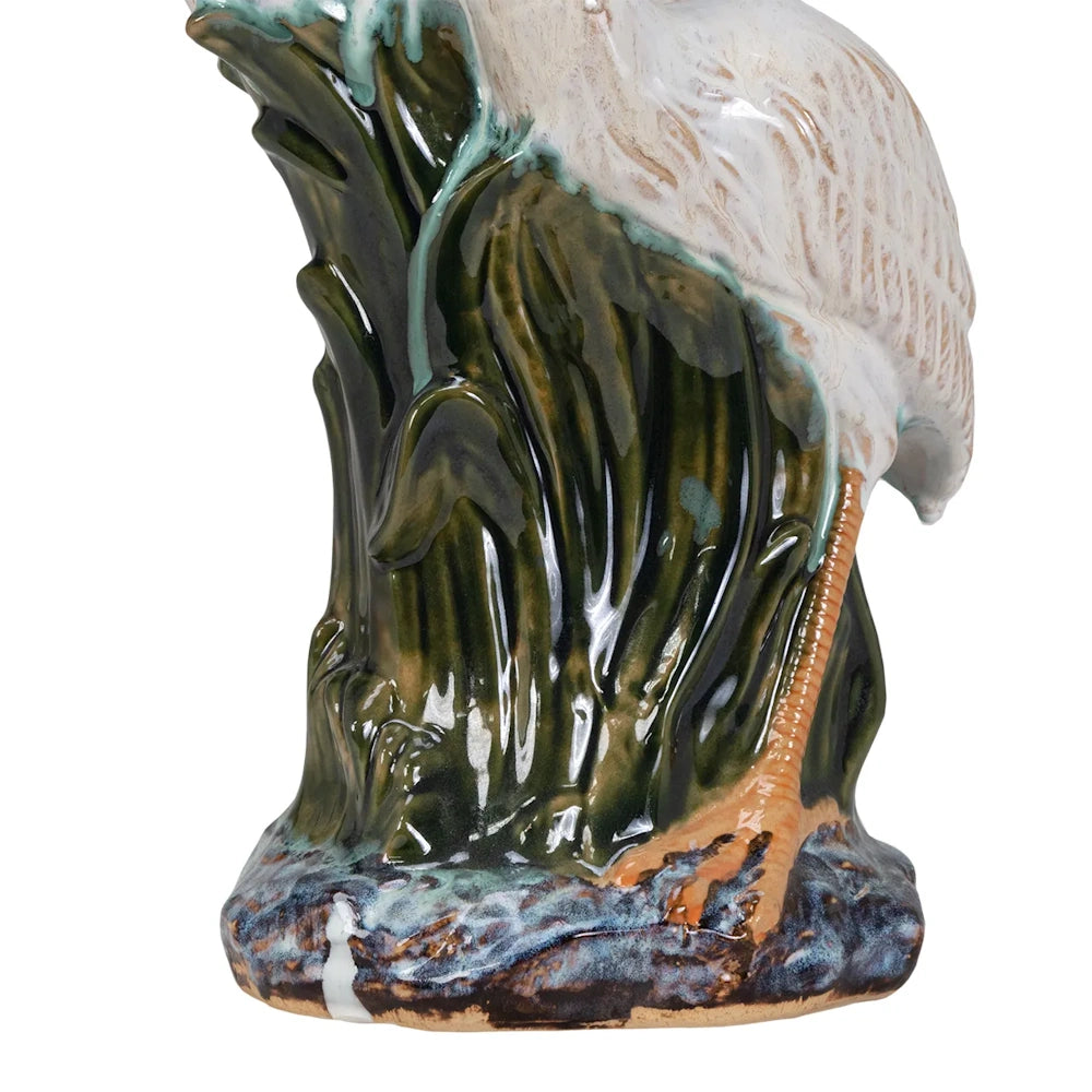Bottom of a ceramic heron figurine featuring a glossy green reed base and a textured white feather body.